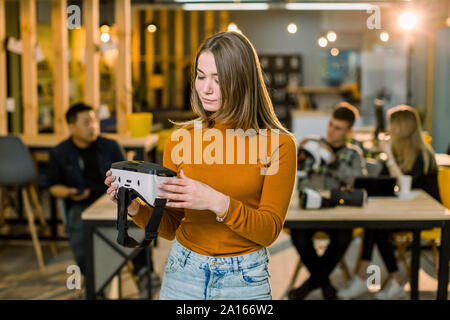 cheerful young woman adjusting her virtual reality headset while standing at her working place in office with relax. Stock Photo