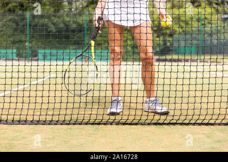 Female tennis player legs on grass court seen through the net Stock Photo