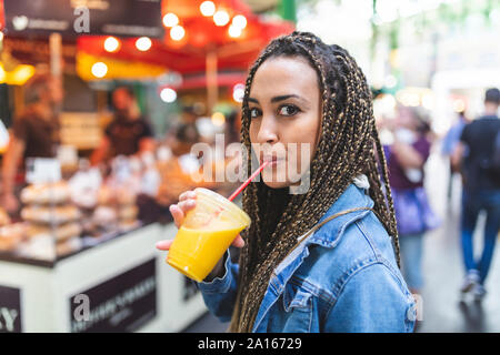 Portrait of young woman drinking fresh orange juice on street market, London, UK Stock Photo