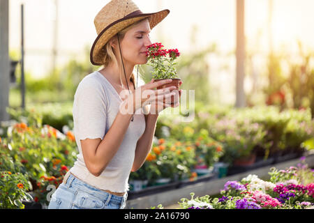 Beautiful young woman smelling at flower in the greenhouse Stock Photo