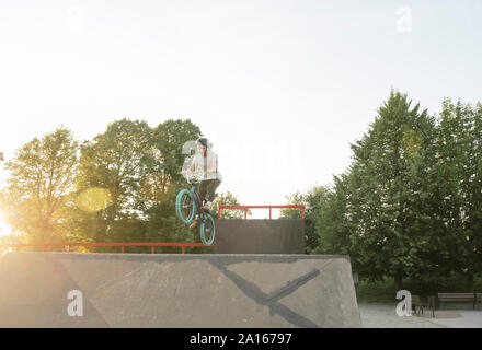 Young man riding BMX bike at skatepark at sunset Stock Photo