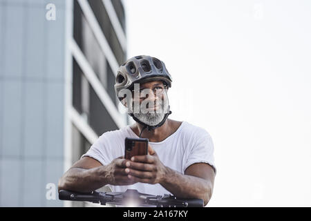 Portrait of happy mature man wearing cycling helmet leaning on handlebar of Electric Scooter Stock Photo