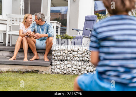 Happy parents sitting on steps in garden with boy in foreground Stock Photo