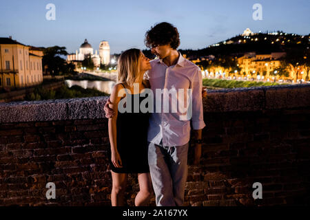 Young couple in love embracing on a bridge at night, Verona, Italy Stock Photo
