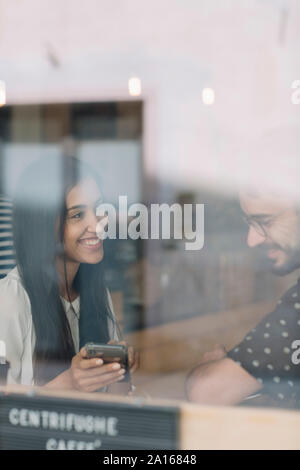 Young couple with smartphone behind windowpane in a cafe Stock Photo