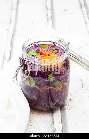 Jar of red cabbage, chili peppers, carrots and coriander on wooden table Stock Photo