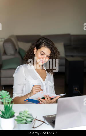 Young woman taking notes at desk at home Stock Photo