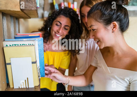 Three smiling young women at a bookshelf Stock Photo