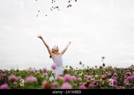 Girl standing in clover field, throwing flowers Stock Photo