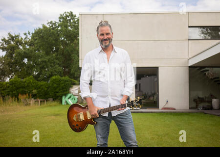 Portrait of mature man standing on lawn in front of his house holding guitar Stock Photo