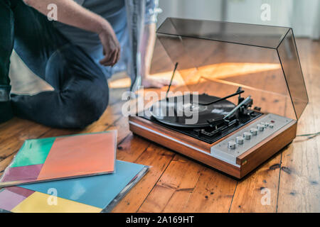 Close-up of man sitting on the floor at home with a record player Stock Photo