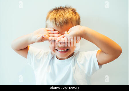 Boy covering his eyes in front of white background Stock Photo