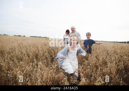 Portrait of happy girl running in an oat field while brother, grandmother and grandfather following her Stock Photo