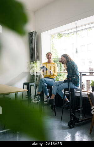 Friends sitting in coffee shop, using digital tablet, e-scooter leaning on table Stock Photo