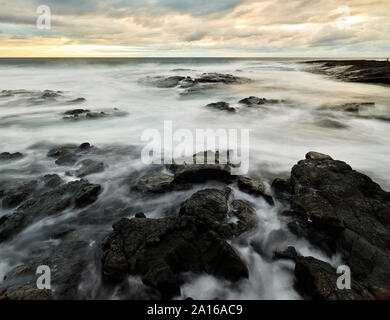 Volcanic rocks amidst water at Puuhonua O Honaunau National Historical Park against cloudy sky during sunset Stock Photo