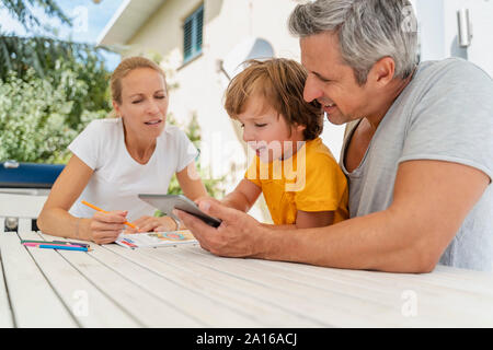 Father, mother and son doing homework and using tablet together on terrace Stock Photo