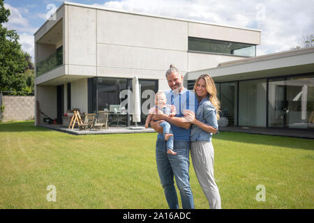 Portrait of happy family of three standing in garden of their home Stock Photo