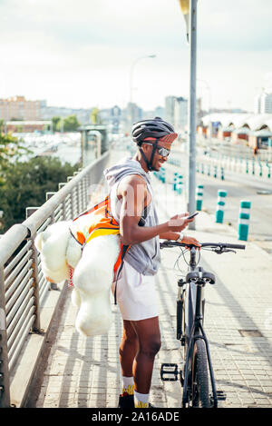 Happy bicycle courier with cell phone and teddy bear Stock Photo