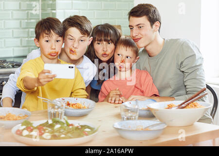 Mother and her four sons taking smartphone selfies at lunch, with faces full of tomato sauce Stock Photo