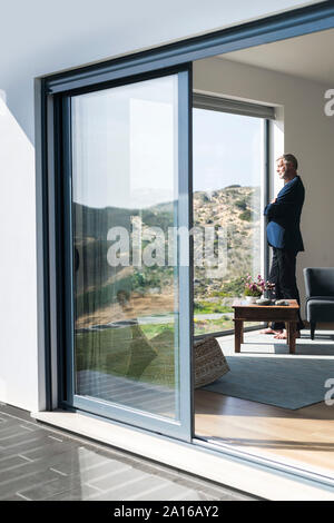 Senior businessman standing at panorama window looking out Stock Photo
