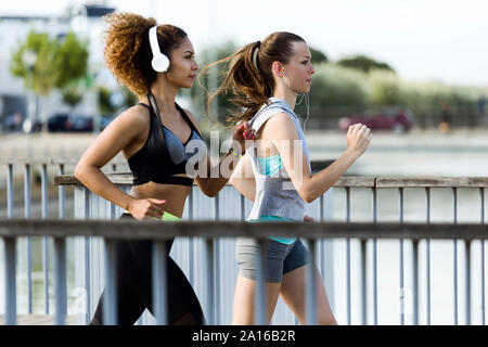 Two sporty young women running on a bridge