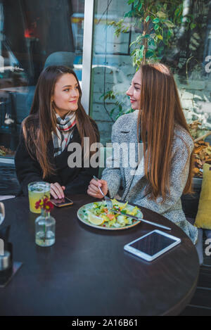two girlfriends talking while eating in outdoors cafe autumn time Stock Photo