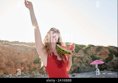 Carefree young woman holding watermelon slice on the beach Stock Photo
