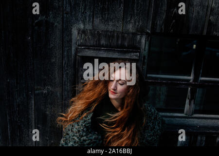 Portrait of redheaded woman with closed eyes, wooden wall in the background