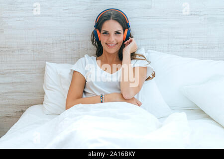 Portrait of smiling young woman lying in bed with headphones