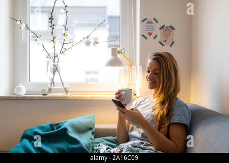 Young woman using cell phone on couch at home Stock Photo