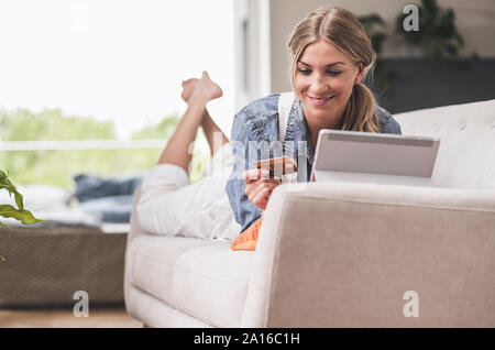 Smiling woman on couch with credit card and tablet Stock Photo
