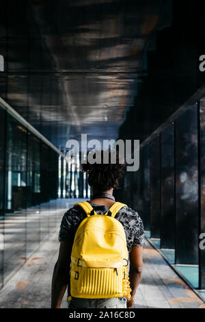 Back view of man with yellow backpack walking through a passage, Barcelona, Spain