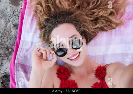 Self portrait of smiling young woman lying on towel on the beach Stock Photo