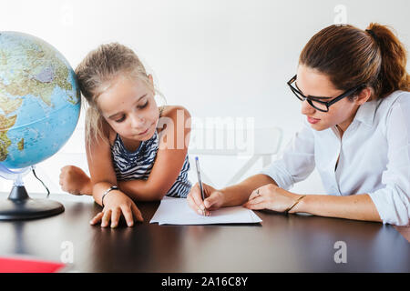 Teacher helping schoolgirl at desk writing on paper Stock Photo