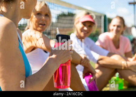 Mature women at tennis club sitting on court taking a break from playing Stock Photo