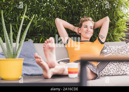 Relaxed woman sitting on couch on terrace at home leaning back Stock Photo
