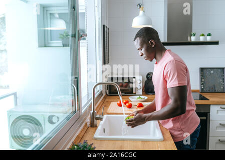 Young man washing lettuce in kitchen Stock Photo