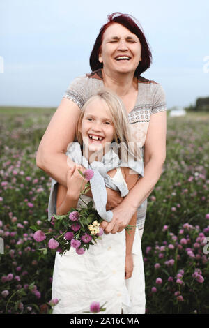 Portrait of laughing grandmother and granddaughter with pickes flowers on a meadow Stock Photo
