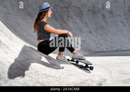 Young woman with skateboard sitting in skatepark Stock Photo