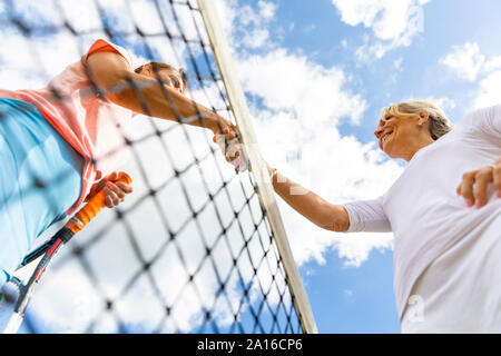Mature women finishing tennis match shaking hands at the net Stock Photo