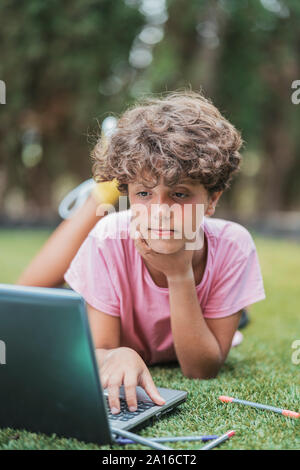 Boy lying in grass using laptop Stock Photo