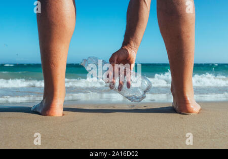 Man standing at seashore picking up empty plastic bottle, close-up Stock Photo