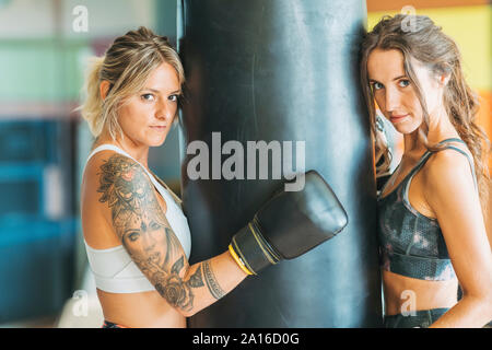 Portrait of two women with boxing gloves at sandbag in gym Portrait of two women with boxing gloves at sandbag in gym