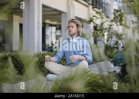Young man meditating outside office building Stock Photo