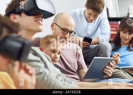 Happy family sitting on couch, using VR goggles and mobile devices Stock Photo