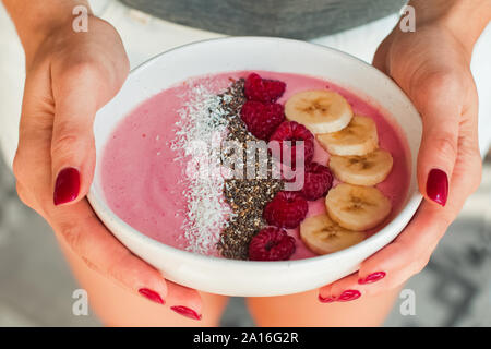 Woman's hands holding smoothie bowl with raspberries and bananas close-up. Stock Photo