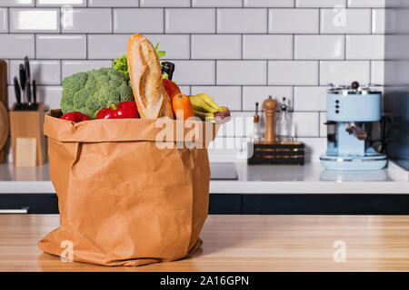 Paper bag full of products from standing on the wooden table with the modern kitchen interior on the background Stock Photo