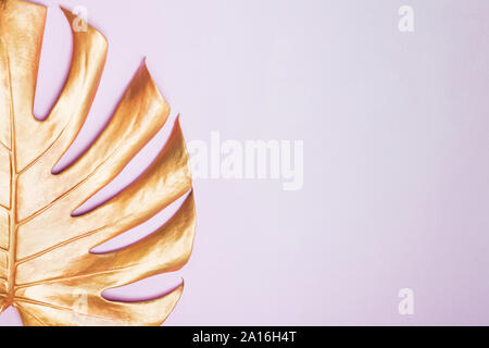 Decorative golden painted leaf of monstera plant on pink background Stock Photo