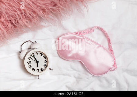 Alarm clock and pink slipping mask on the bed, Stock Photo