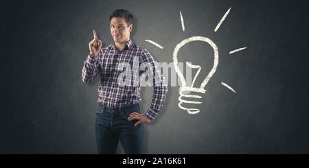 young man in front of chalkboard with light bulb drawn on it has an idea Stock Photo